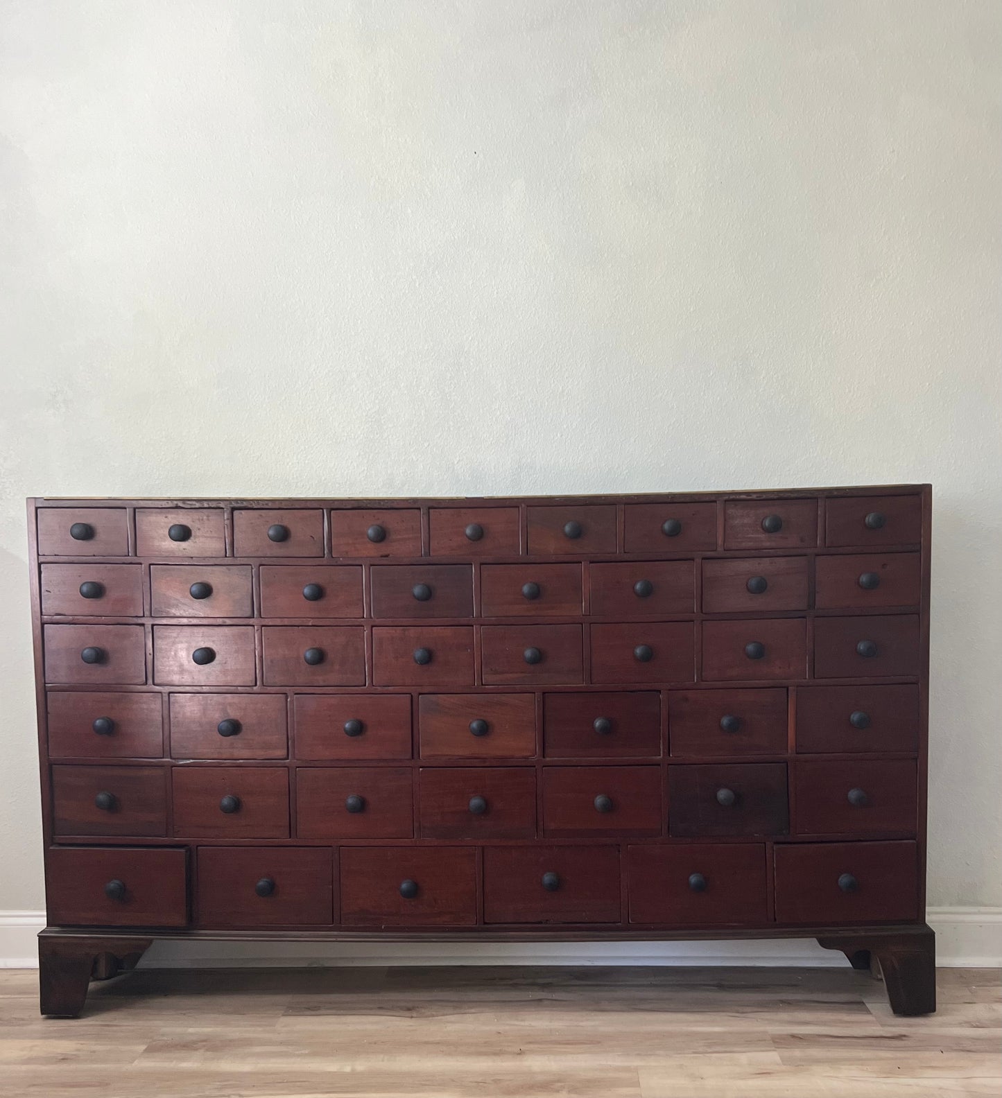 Wooden apothecary cabinet with multiple drawers against a plain wall.